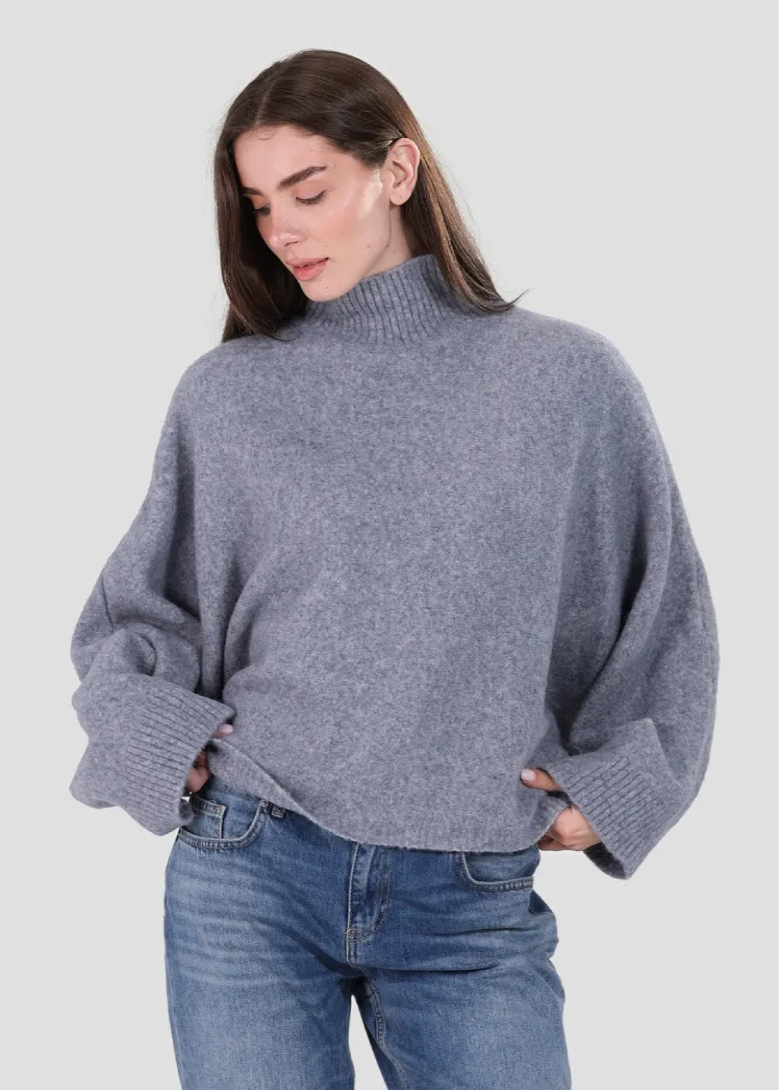 Woman wearing a gray sweater and blue jeans on a light gray background