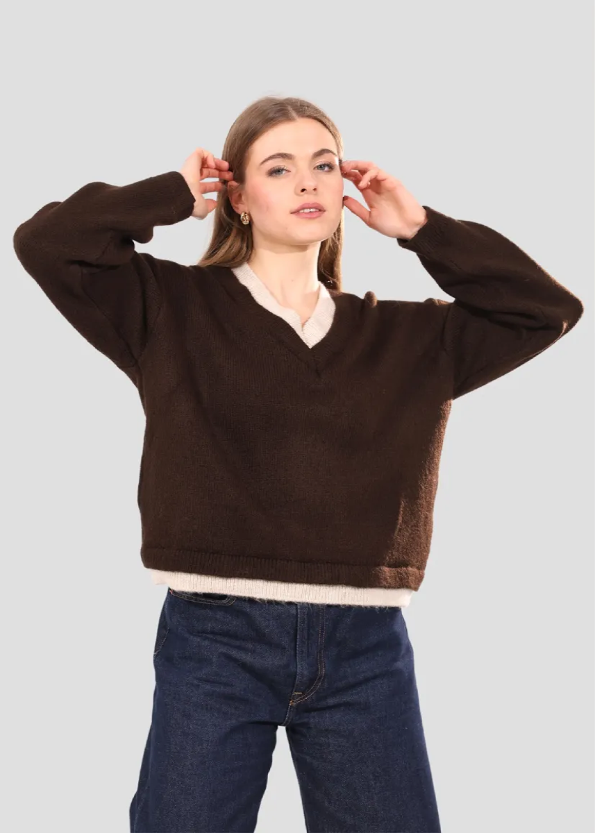 Person wearing a brown sweater with a white collar and blue jeans on a light gray background