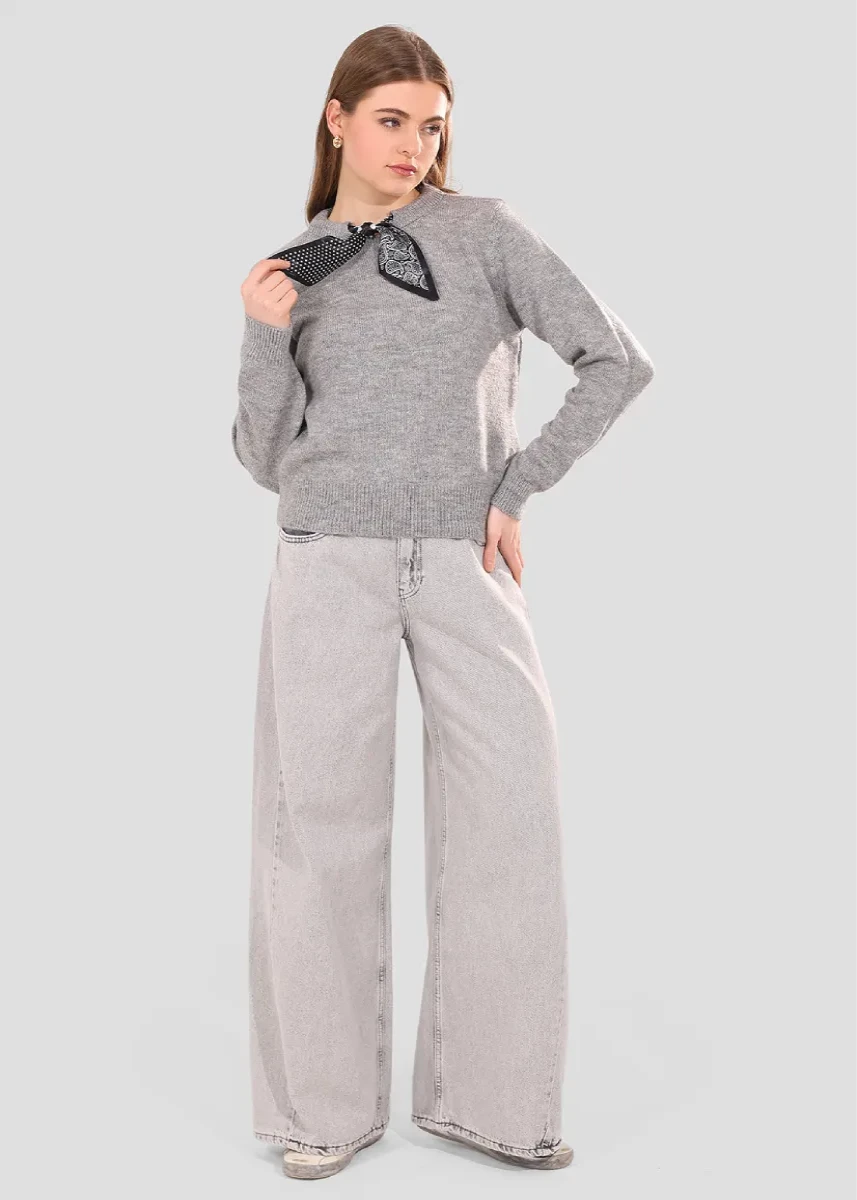 Woman wearing a gray sweater and wide-leg jeans on a light gray background